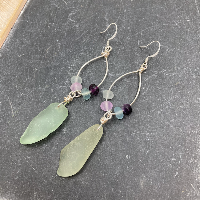 Earrings with light green sea glass drops and fluorite rounds on oval silver forms. 
