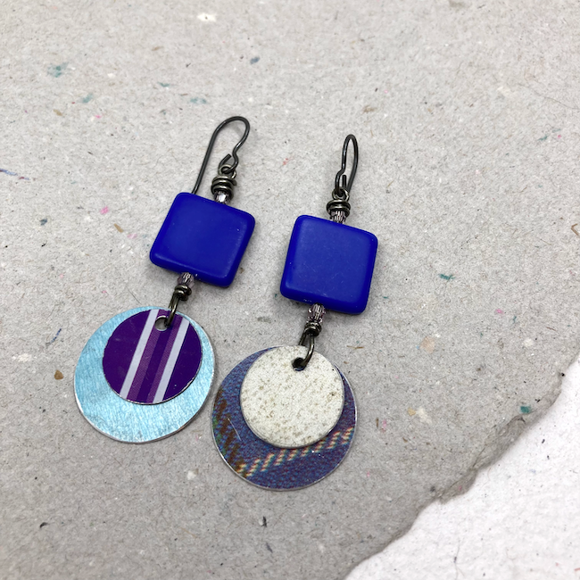 Earrings with mismatched blue, purple and silver tin layered rounds and bright blue square glass beads. 