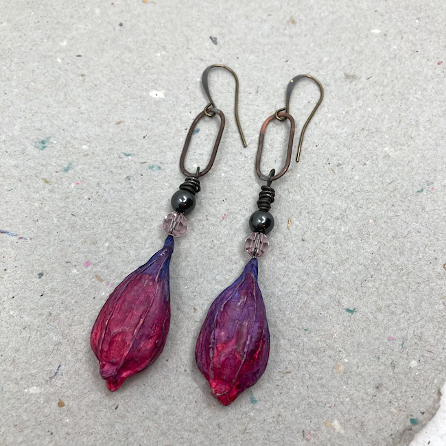 Earrings with pink/purple polymer pod drops with crystal and pearls hanging from patina copper ovals. 