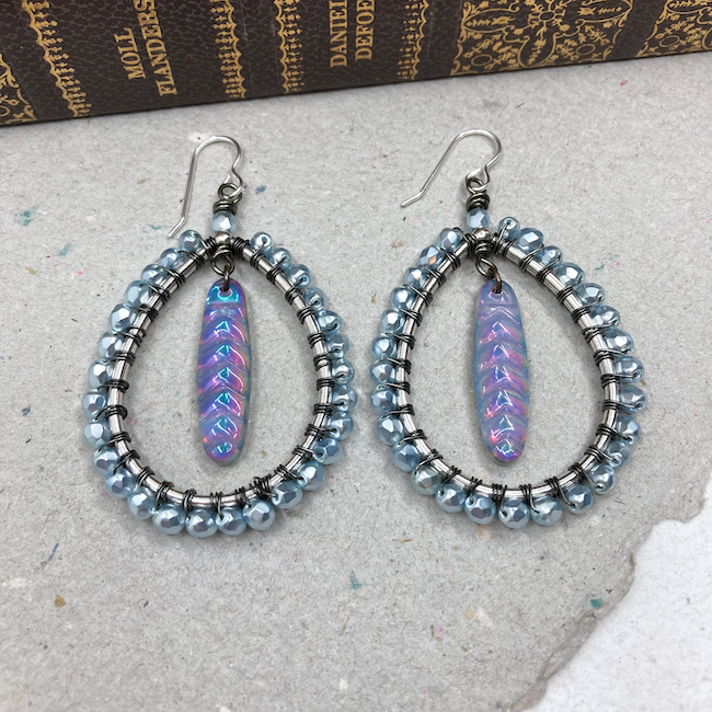Earrings with small blue wire wrapped beads around the edge of oval forms and purple/blue long dangles in the middle.