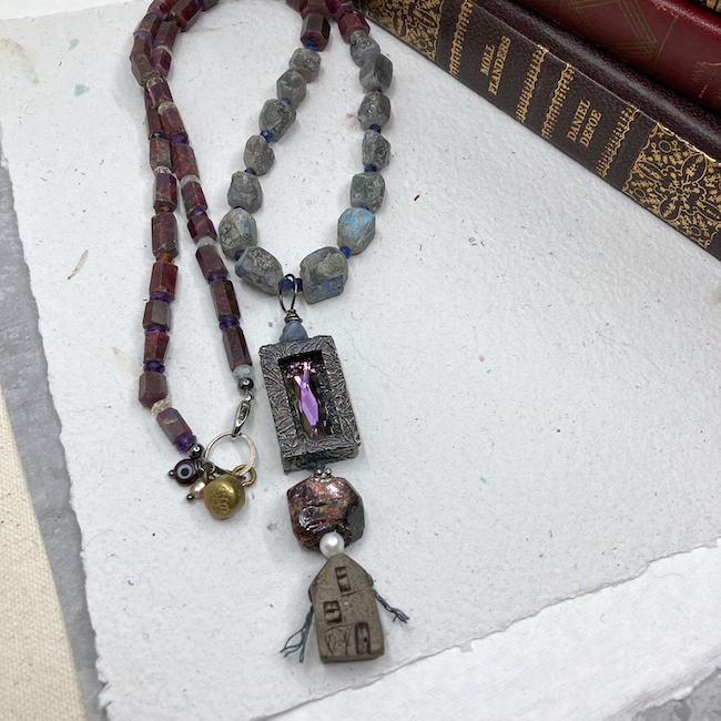 Necklace with pendant of a house, vintage garnet, textured metal shrine with crystal, rough sapphire, rough tourmaline, ruby in zoisite, tiny sodalite and mixed gemstone spacers. On the clasp are an "eye" bead, tiny vintage pearl and brass button with lotus design. 