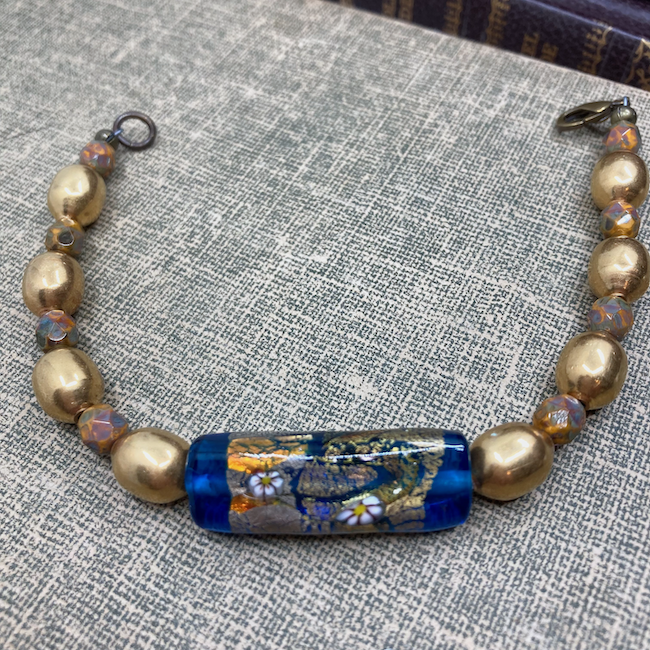 Bracelet with blue glass bracelet bar with gold foil, millefiore type flowers, and orange with large metal beads and small brown and orange Czech glass spacers. 