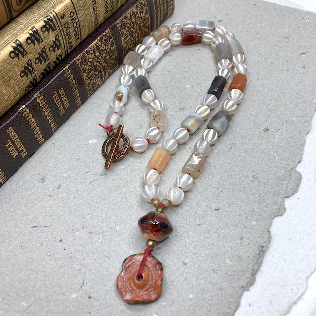 Necklace with white, peach, and grey beads, rusty tone lampwork beads for a pendant and a copper toggle clasp. 
