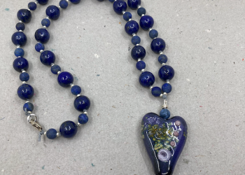 Necklace with blue floral glass heart pendant and variety of blue beads with silver spacers.