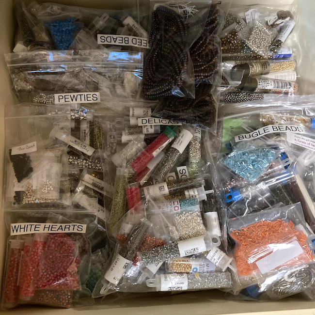 Drawer of large numbers of sizes, shapes, and colors of seed beads with labels. 
